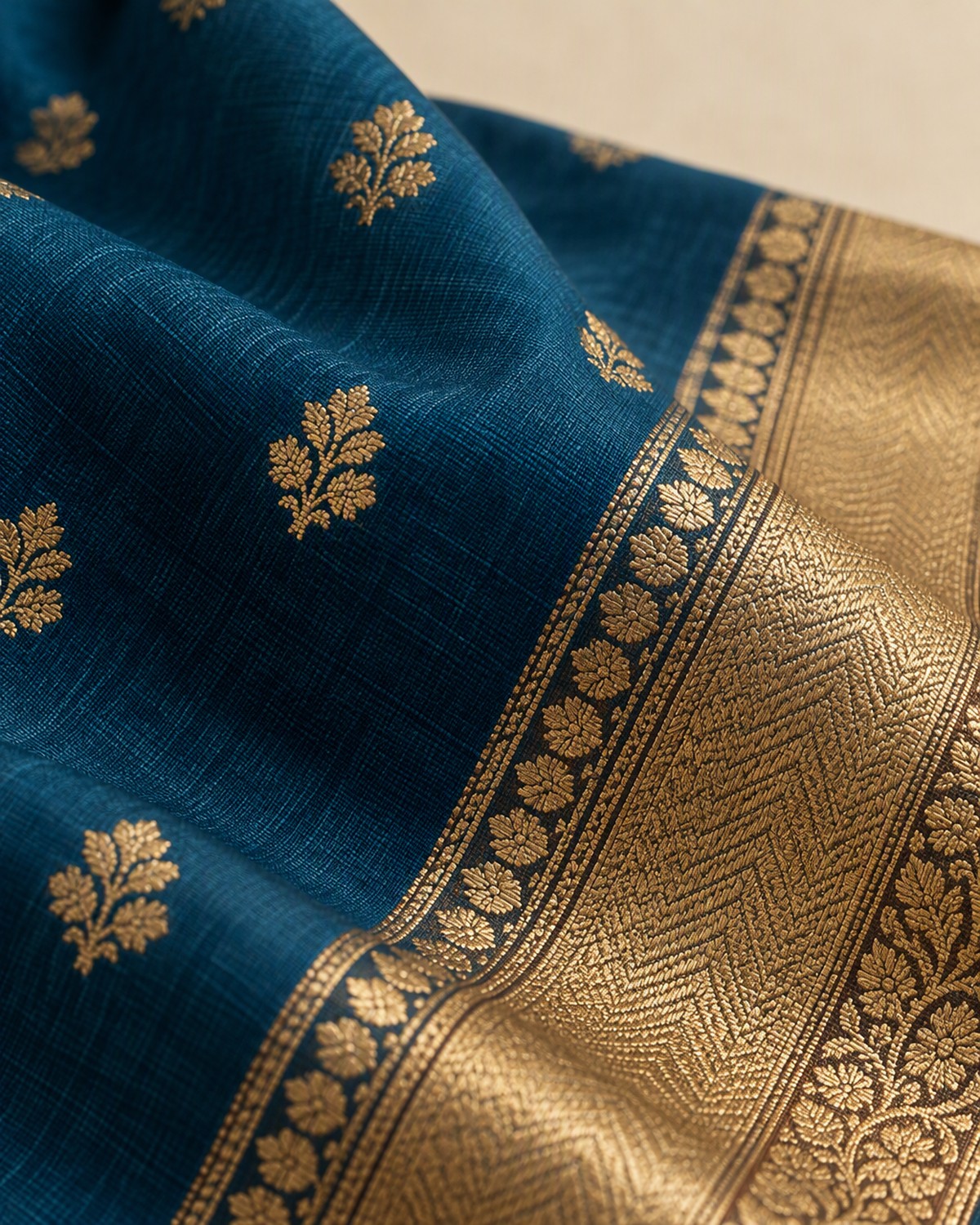 Close view of the peacock blue saree fabric showing a gold floral motif and the gold border edge