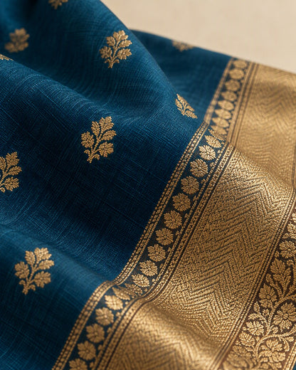 Close view of the peacock blue saree fabric showing a gold floral motif and the gold border edge